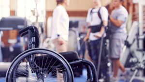 Spinal cord injury patient leaning to walk while the wheelchair sits in the foreground.