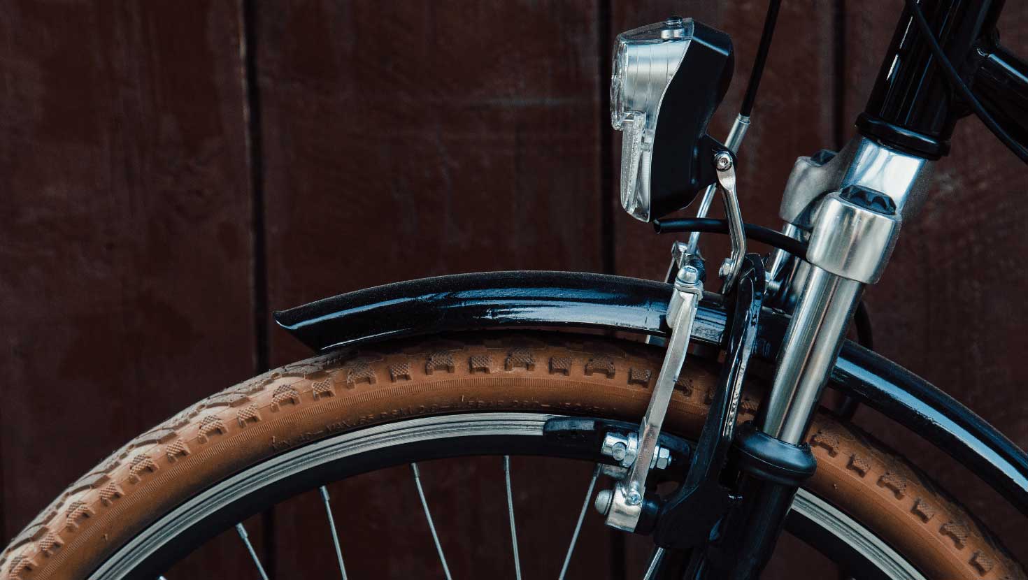 A close up of the front bicycle tire and handlebars up against a wall