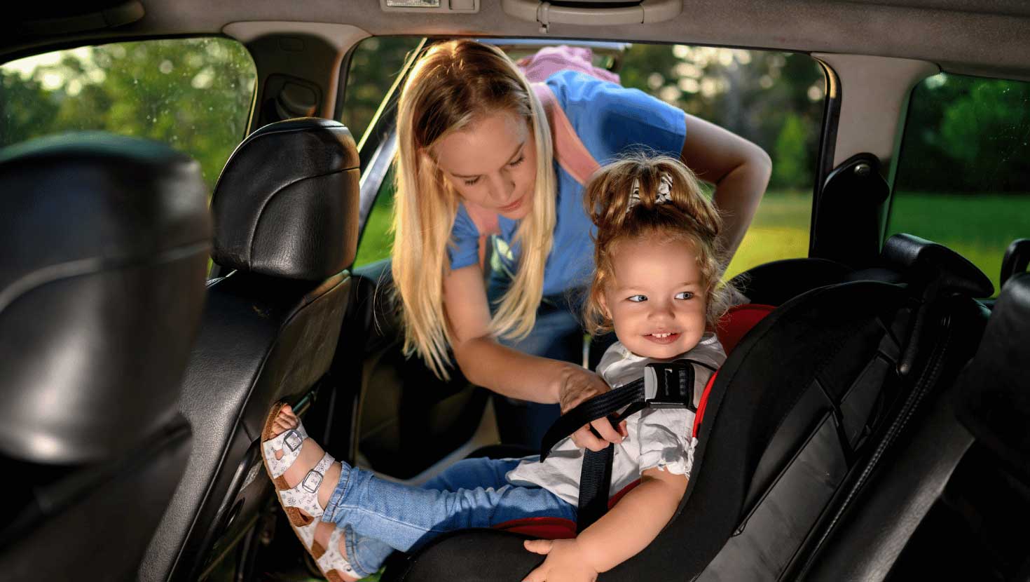 Mother straps her smiling toddler daughter into a car seat.
