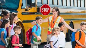 School bus driver helping children across the street in front of the bus.
