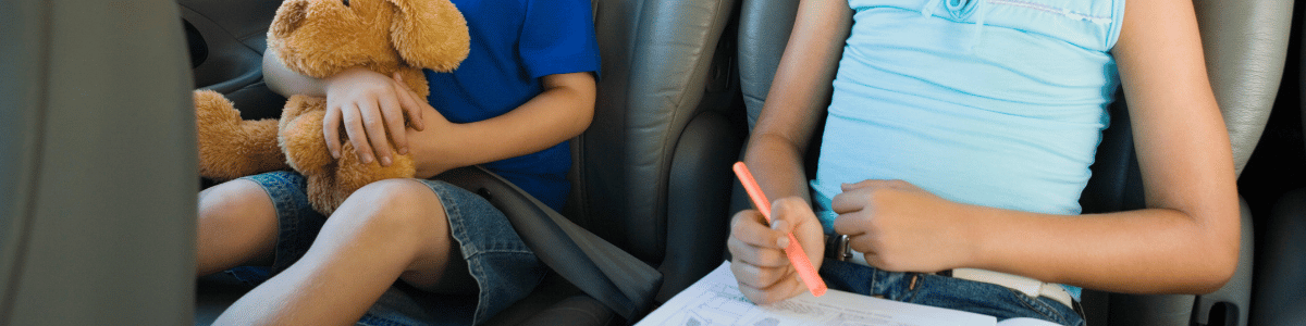 Children sitting quietly in thebackseat of a vehicle playing with a toy and colouring in a book.