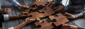 Hands putting various big wooden puzzle pieces together at a table