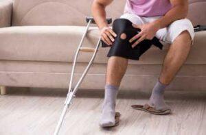 A man putting on a knee brace with a crutch beside him
