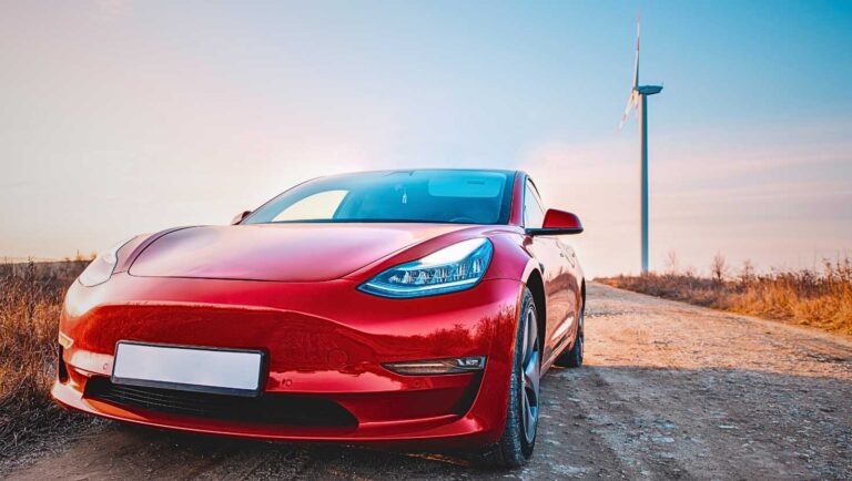 Picture of a Tesla car on a dirt road by a wind mill