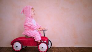Toddler in a pink bunny onesie driving a toy car